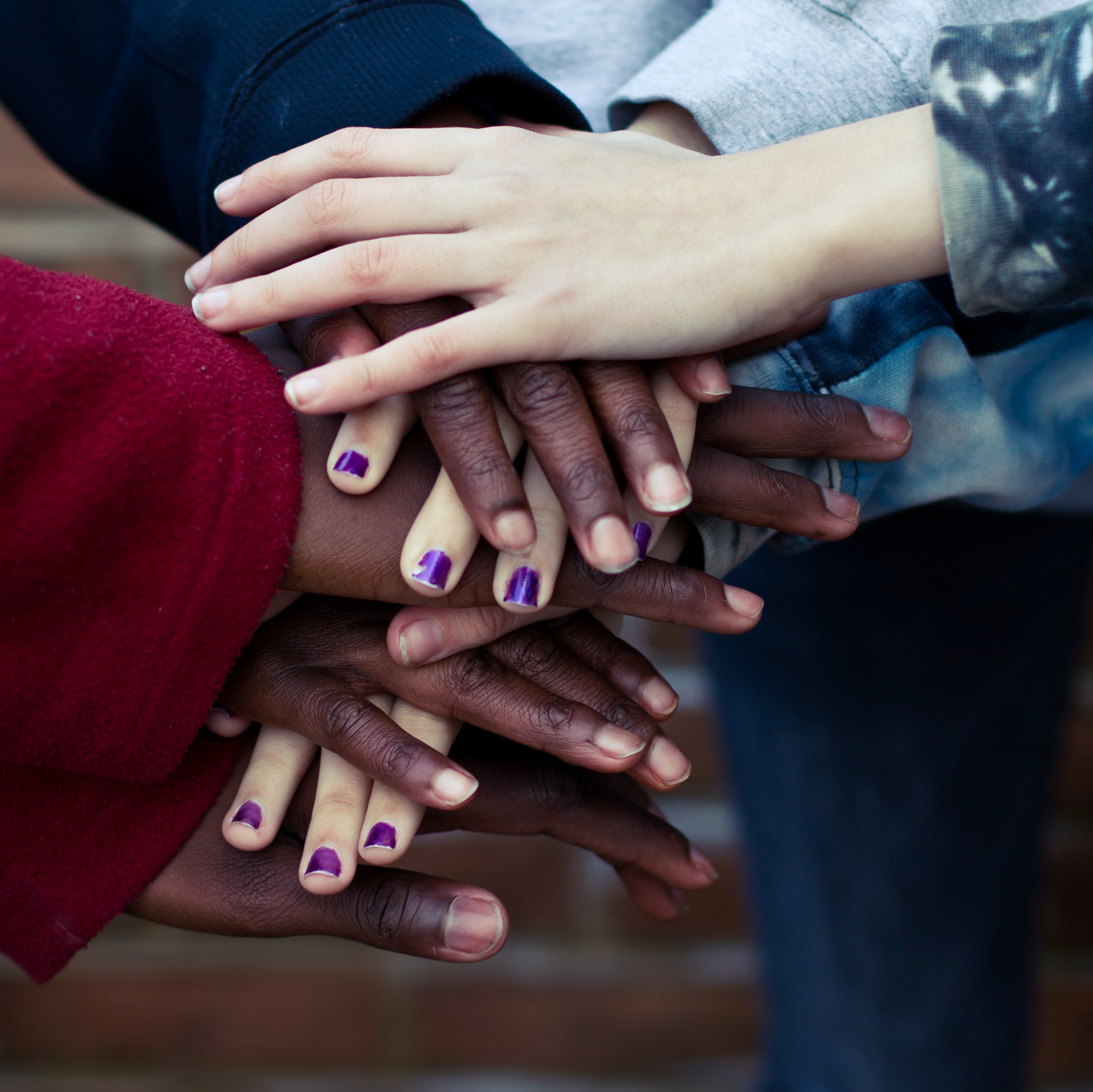 Close up on a set of hands of various skin tones stacked on top of each other