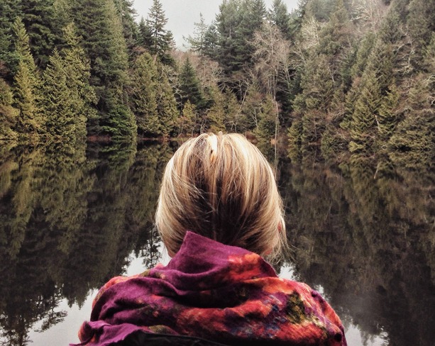 Back of womans head looking out over a pond with pine trees on an overcast day