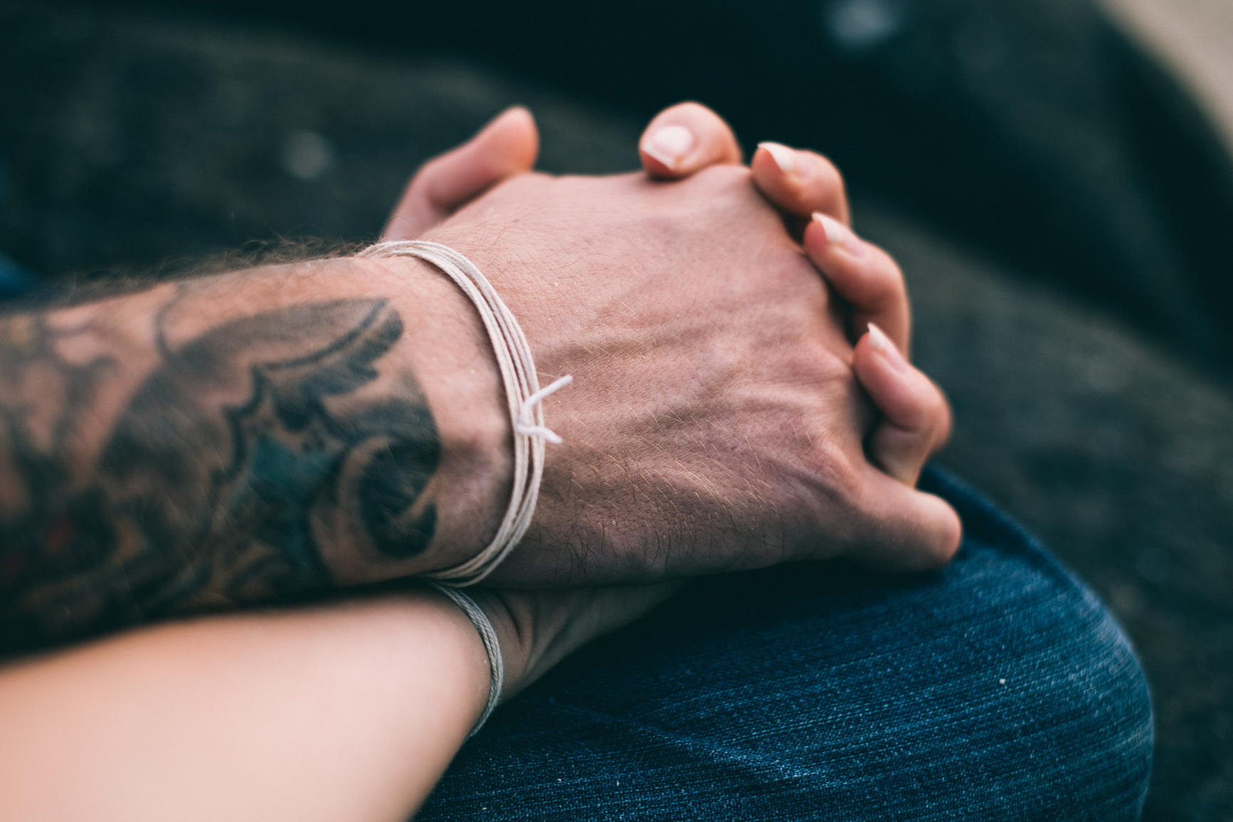 Two hands clasped together wearing similar string bracelets