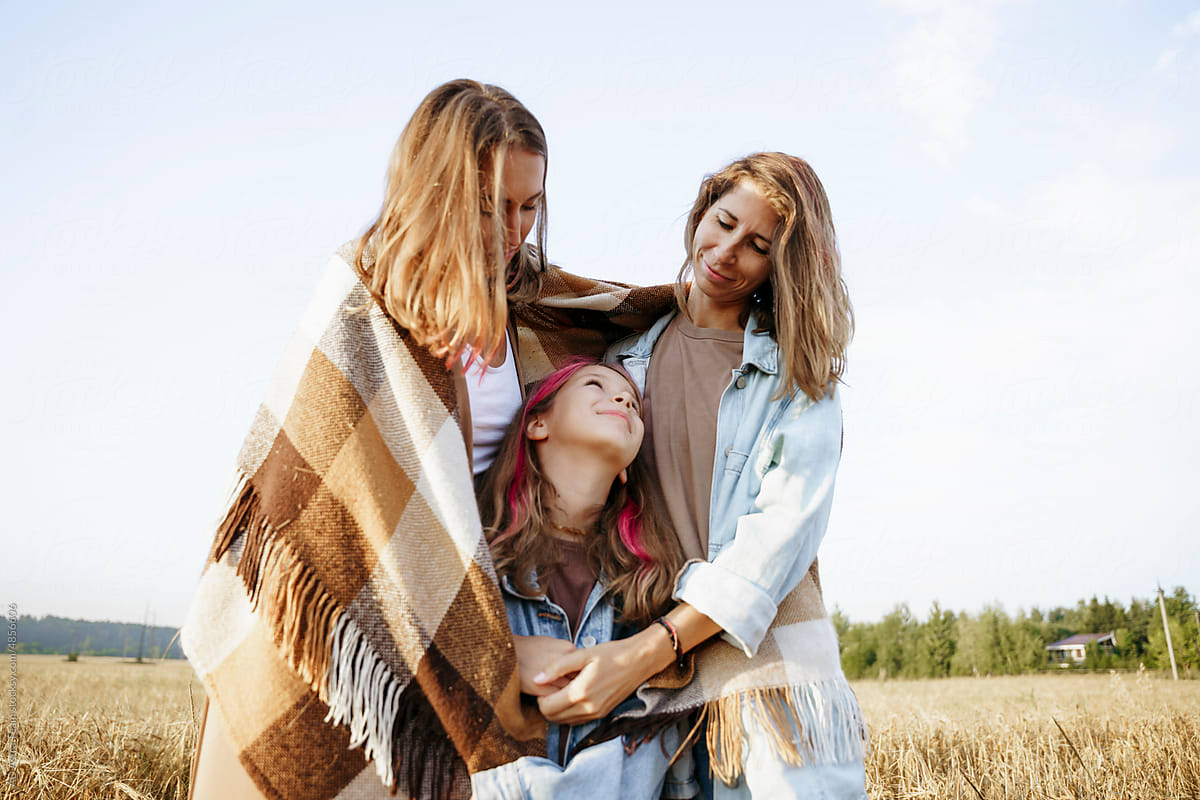 Mothers and their daughter cover themselves with a blanket and hug